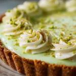 A beautifully baked pistachio cream pie topped with whipped cream and crushed pistachios on a rustic wooden table