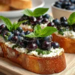 A delicious platter of basil blueberry ricotta bruschetta topped with fresh basil leaves and blueberries