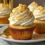 A plate of golden angel food cupcakes topped with fluffy white frosting and colorful sprinkles