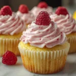 A beautifully decorated lemon cupcake topped with vibrant raspberry buttercream frosting and fresh raspberries.